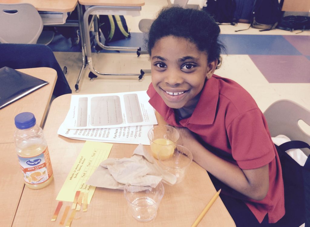 A student tutee with the DC STEM program smiles in the midst of a lab experiment.