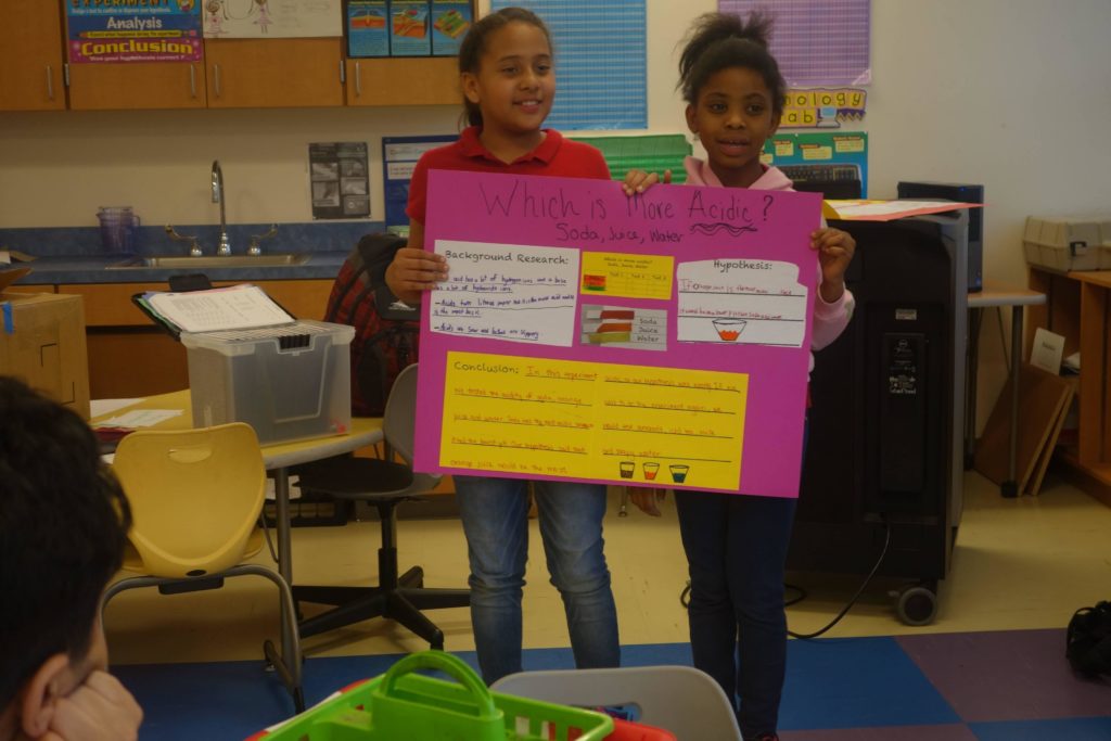 Two student tutees with the DC STEM program hold up a poster presentation they made.