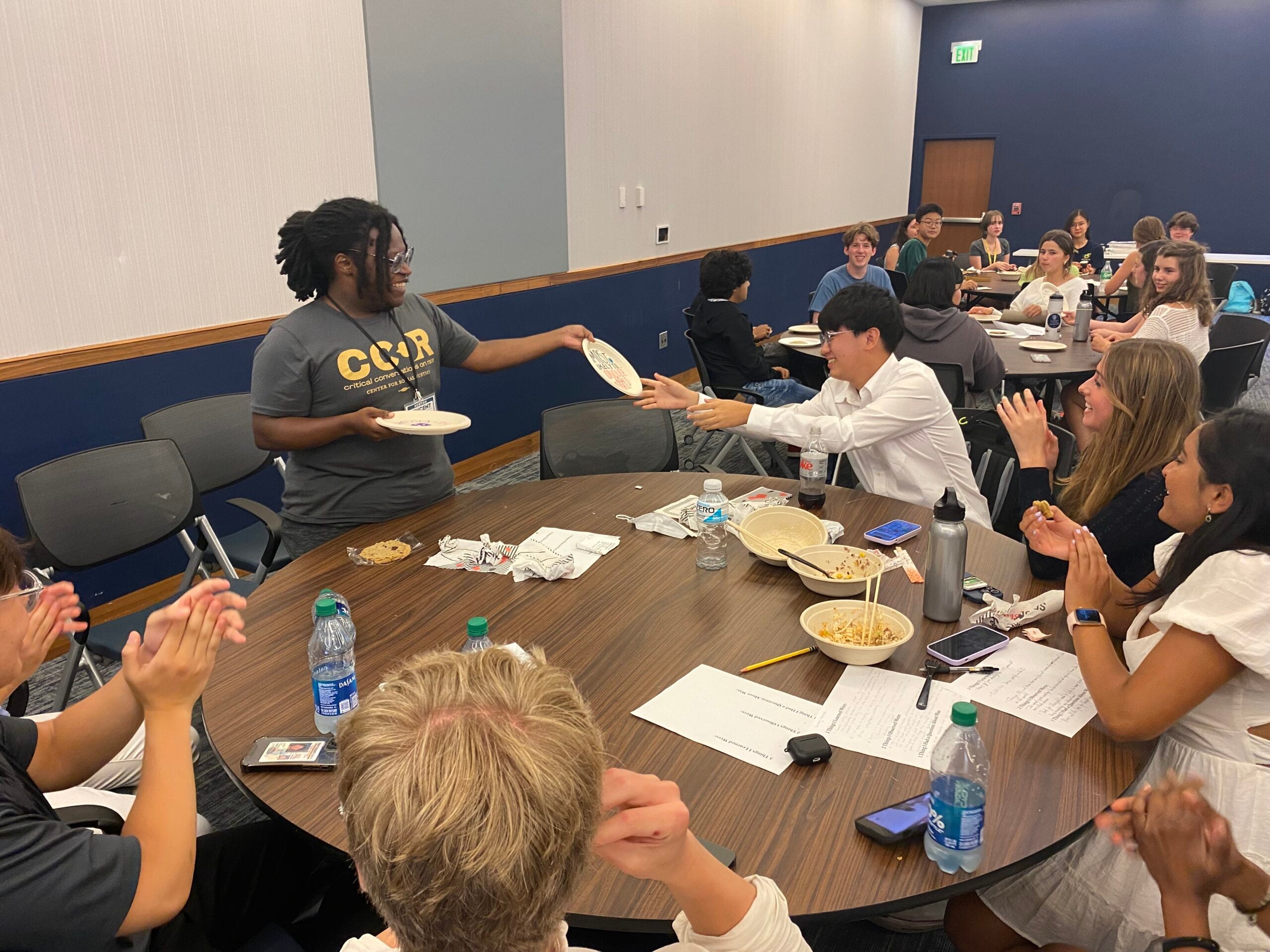 College mentor hands high school a paper plate award during the closing ceremony of Bridges program. Other students clap and smile.