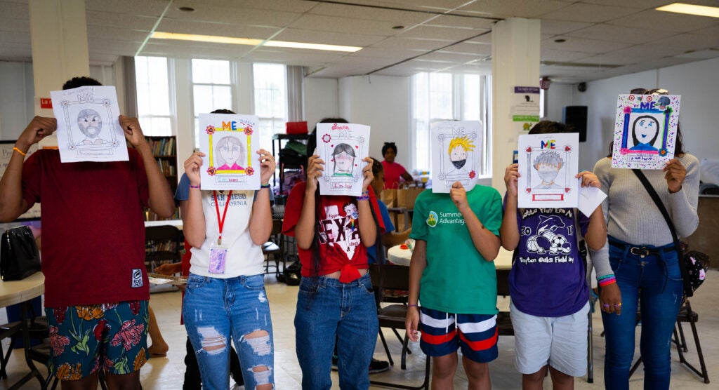 Youth holding self portraits in front of their faces