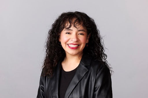 Woman with long dark hair and bangs wearing all black smiling at camera