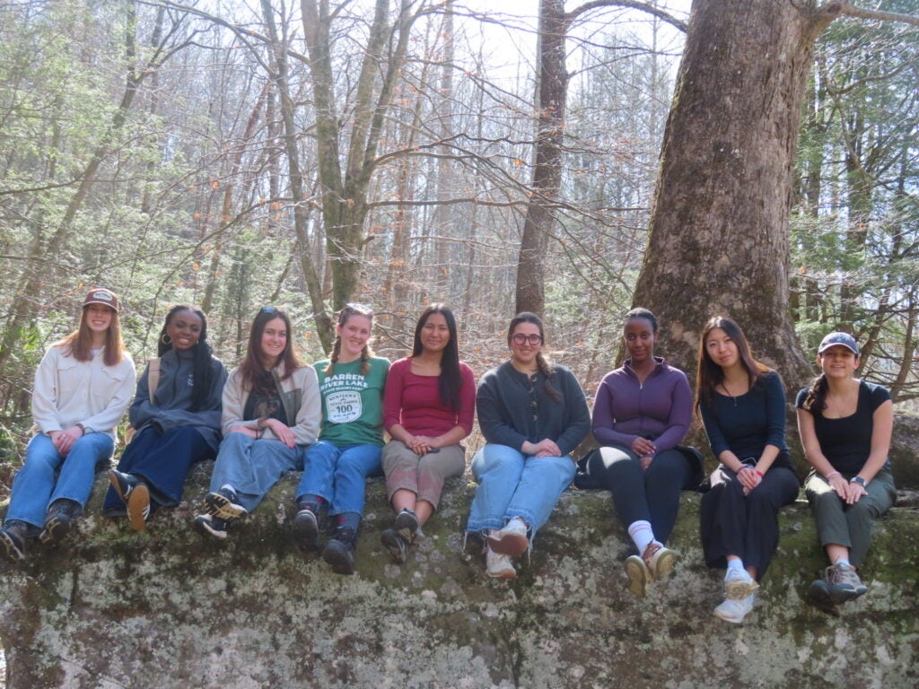 students sitting on a log in the forest
