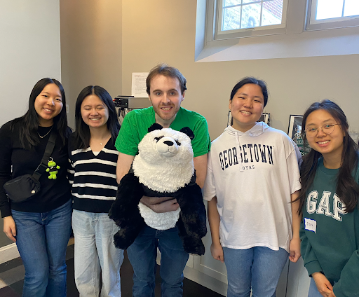 A group of five people smiling and posing with a large stuffed panda bear in a cheerful setting.